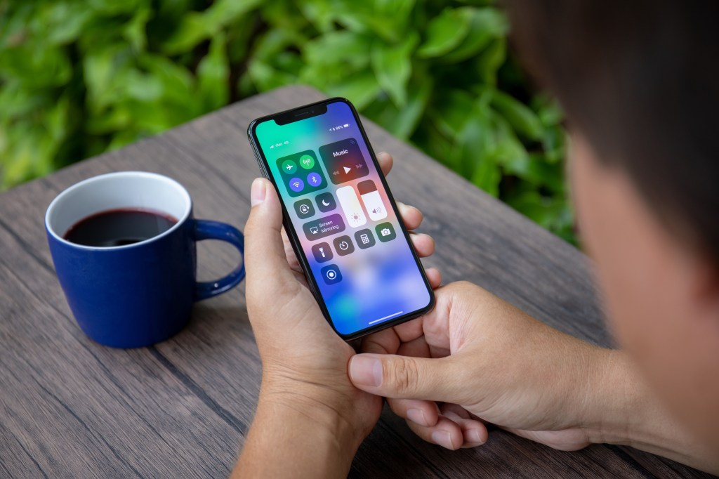 Koh Samui, Thailand - March 26, 2018: Man Hand Holding iPhone X with Home screen control center. The iPhone 10 was created and developed by Apple Inc.